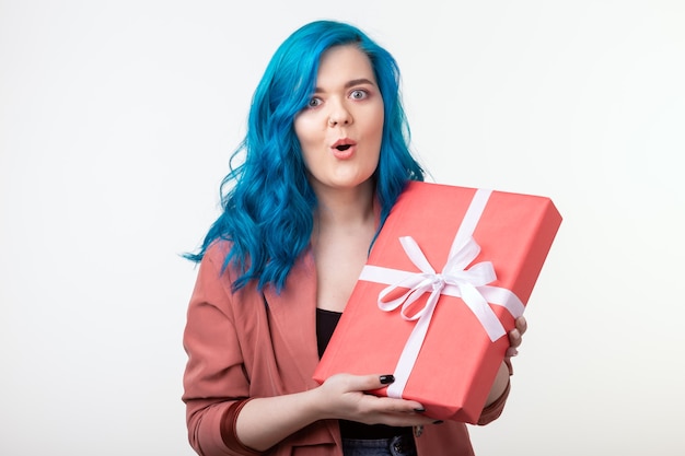 Concepto de personas, vacaciones y moda - Mujer sorprendente con cabello azul sosteniendo una caja de regalo en blanco