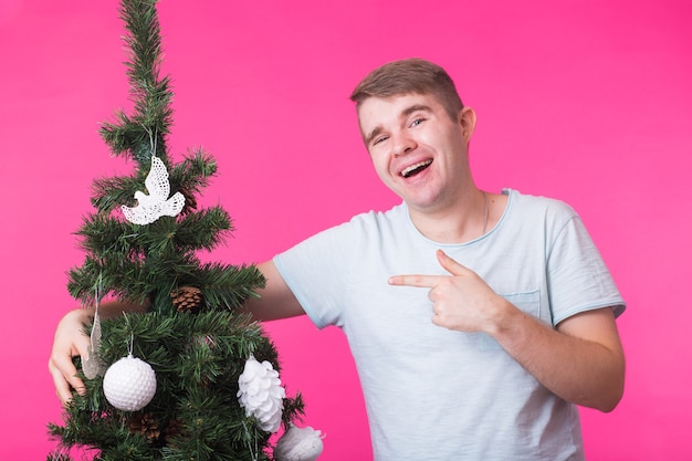 Concepto de personas, vacaciones y Navidad - joven decorar el árbol de Navidad sobre fondo rosa