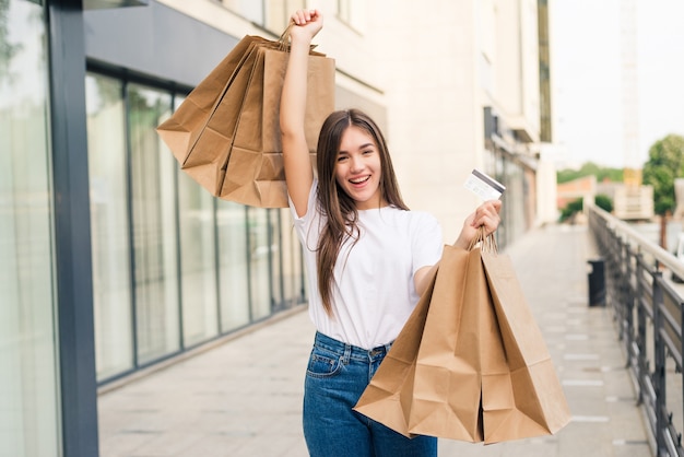 Concepto de personas, venta y consumismo - cerca de mujer feliz con bolsas de compras y tarjeta de crédito en las calles de la ciudad