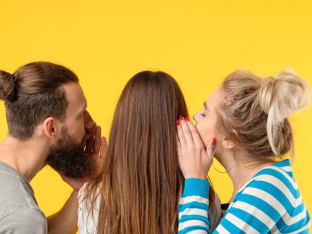 Concepto de persuasión. Hombre y mujer susurrando al oído de las niñas. Copie el espacio en la pared amarilla.