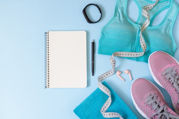 Concepto de plan de entrenamiento. Elegantes equipos deportivos para mujeres, ropa, gadgets y libreta en blanco desde arriba