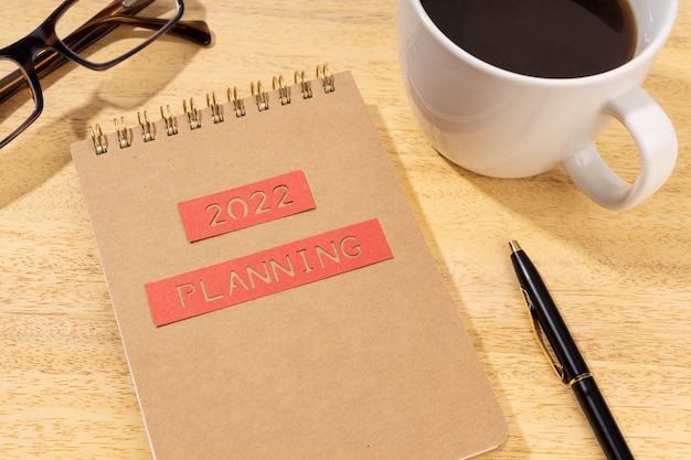 Concepto de planificación de año nuevo 2022. Bloc de notas, taza de café y anteojos en el escritorio de madera