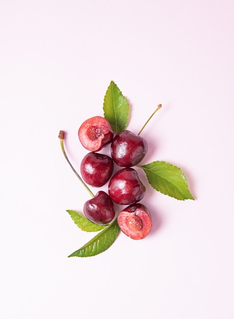 Concepto plano sentar con unas jugosas cerezas rojas con hojas verdes sobre un fondo rosa. Vista superior y copia de la imagen del espacio.