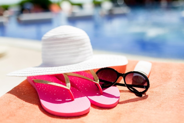 concepto de playa, verano, vacaciones y accesorios - cierre de sombrero, protector solar y gafas de sol en la piscina