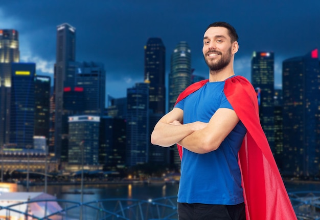 Foto el concepto de poder y gente: hombre feliz con capa roja de superhéroe durante la noche rascacielos de la ciudad de singapur en el fondo