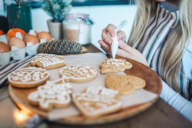 Foto concepto de preparación y creatividad de vacaciones de navidad año nuevo preparándose para la celebración manos de mujer decorando galletas de jengibre caseras con glaseado