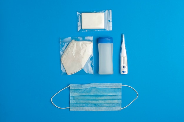 concepto de prevención del coronavirus, gel con tapón azul, termómetro digital, máscara azul, máscara blanca en bolsa protectora individual