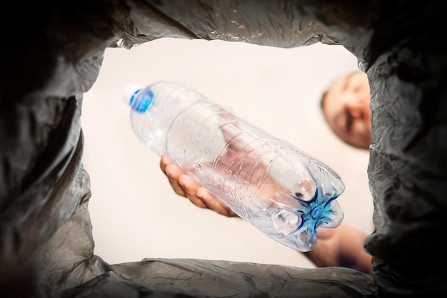 Concepto del problema de la eliminación de residuos plásticos. Un hombre arroja una botella vieja usada en un bote de basura negro. Residuos de botellas de plástico, para reciclaje