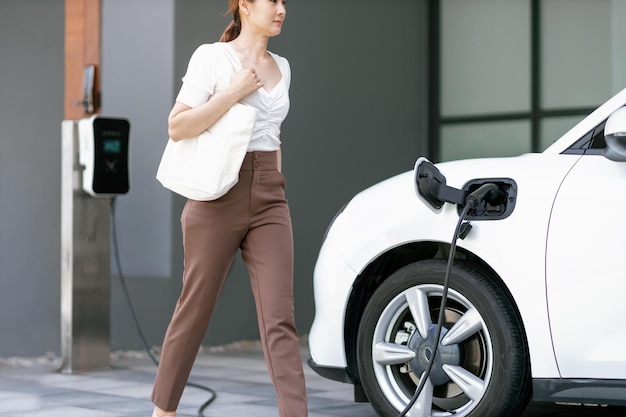 Concepto progresivo de mujer asiática y coche eléctrico con estación de carga doméstica