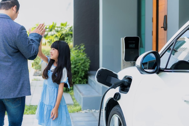 Concepto progresivo de padre e hija con coche EV y estación de carga doméstica