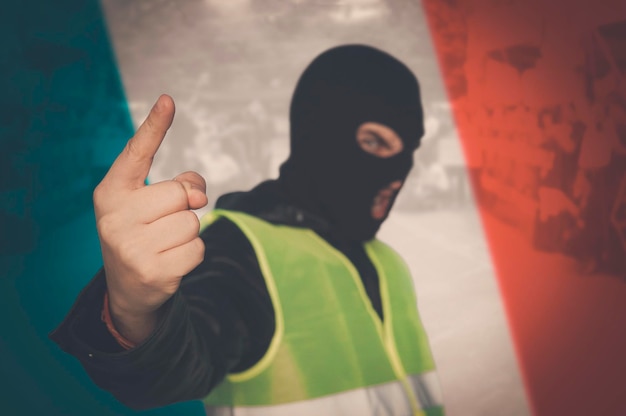 Concepto de protestas callejeras de trabajadores proletarios contra el sistema burgués Chalecos amarillos protestan contra el aumento de los precios del combustible en Francia hombre con una máscara y un chaleco amarillo sobre el fondo de la bandera francesa