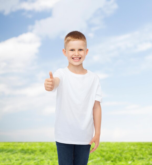 concepto de publicidad, gente, verano e infancia - niño sonriente con camiseta blanca mostrando los pulgares hacia arriba sobre el fondo natural