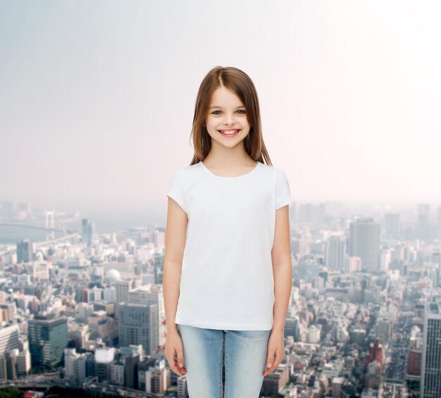 concepto de publicidad, infancia y personas - niñita sonriente con camiseta blanca en blanco sobre el fondo de la ciudad