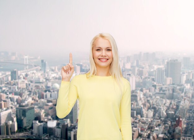 concepto de publicidad - mujer joven atractiva con ropa informal apuntando con el dedo hacia arriba