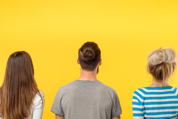 Concepto de publicidad. Vista posterior de tres personas mirando un objeto imaginario. Copie el espacio en la pared amarilla.