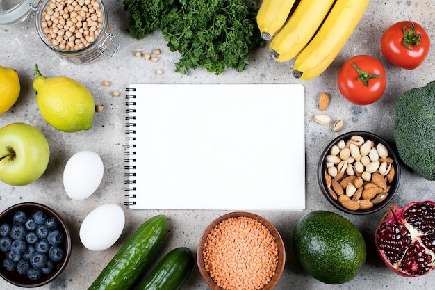 Concepto de receta de maqueta de alimentos. Vegetales verdes, tomates, nueces, frutas, lentejas, garbanzos, verduras y cuaderno vacío en blanco sobre mesa de concreto gris. Plano, vista superior, espacio de copia