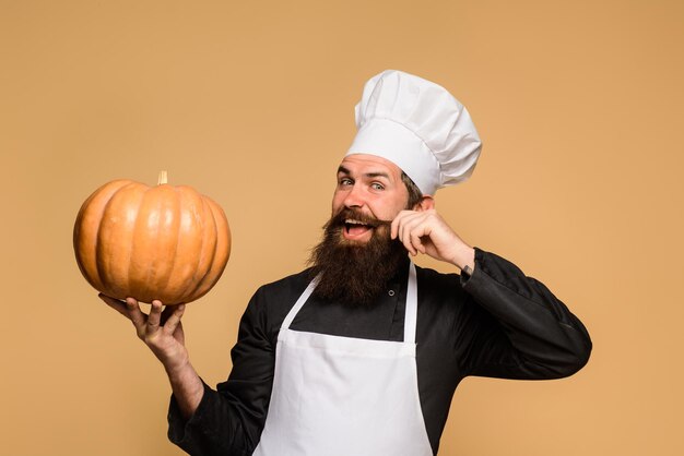 Concepto de recetas de otoño feliz halloween hombre barbudo cocinero con sombrero de chef con verduras útiles de calabaza