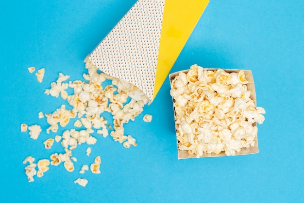 Concepto de refrigerio Palomitas de maíz dulces en un vaso de papel y se derraman del vaso de papel sobre fondo azul claro