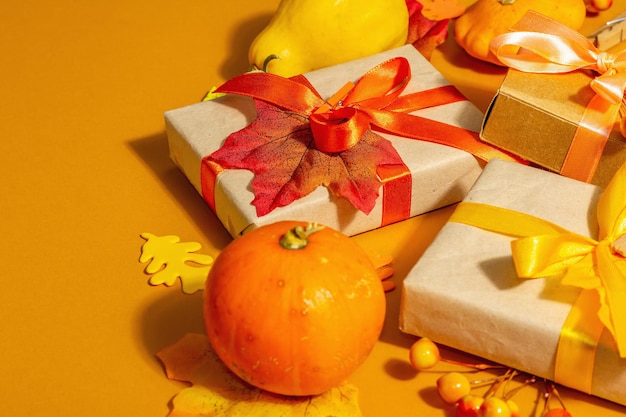 Concepto de regalo en colores otoñales. Cajas envueltas, decoración festiva de otoño, calabaza, hojas y bayas. Una luz dura de moda, sombra oscura, fondo naranja, espacio de copia