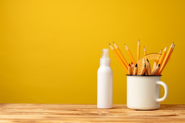 Concepto de regreso a la escuela con artículos de papelería en taza y spray antiséptico de mano en amarillo