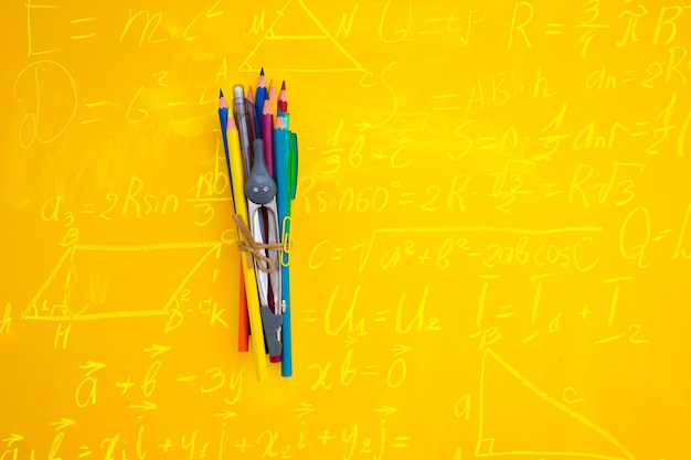 Concepto de regreso a la escuela escena minimalista y creativa con herramientas y espacio de copia sobre fondo amarillo con fórmulas matemáticas