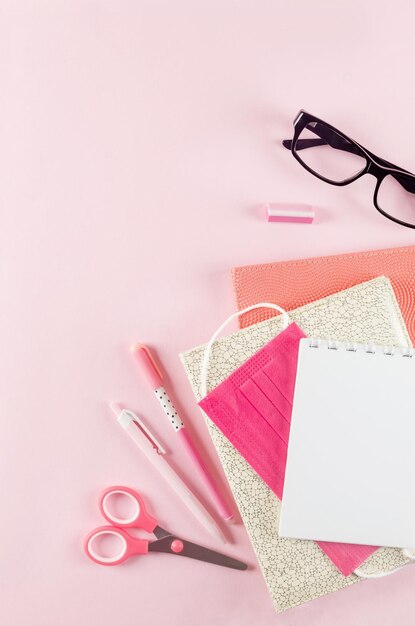 Concepto de regreso a la escuela. material escolar con mascarilla médica sobre fondo rosa. Cuaderno vacío, lápiz y nota adhesiva. escolarización en una pandemia. Copie el espacio, plano.