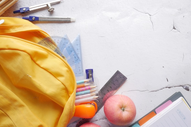 Foto concepto de regreso a la escuela con mochila amarilla y proveedores escolares en la mesa