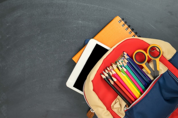 Foto concepto de regreso a la escuela. mochila con útiles escolares, tableta y contra pizarra. vista superior. copia espacio