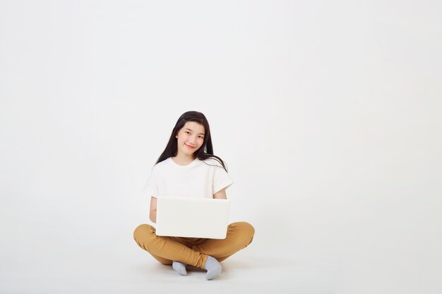 Concepto de regreso a la escuela, mujer asiática joven feliz agradable atractiva sentada en el suelo con las piernas cruzadas y usando la computadora portátil