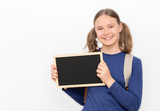 Concepto de regreso a la escuela Niña adolescente sonriente con una pequeña pizarra y una mochila en el fondo gris