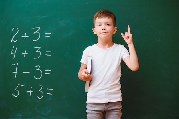 Concepto de regreso a la escuela. Niño de la escuela en clase. Niño feliz contra la pizarra verde. Niño inteligente en el aula. Concepto de idea y educación