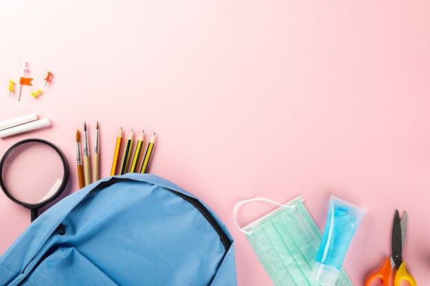 Concepto de regreso a la escuela o la universidad, útiles escolares, mochila de papelería y mascarilla quirúrgica