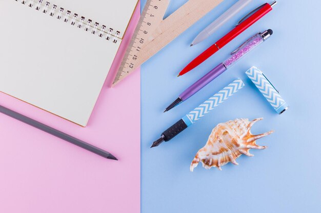 Foto concepto de regreso a la escuela papel de la escuela y conchas marinas en fondo rosa azul lápiz y lápiz