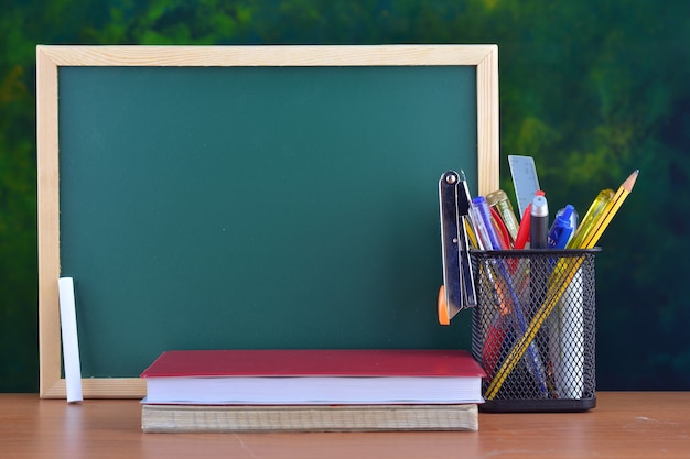 Concepto de regreso a la escuela con papelería en la mesa frente a la pizarra