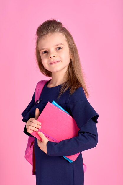 Concepto de regreso a la escuela Retrato de la foto de la mitad de la vuelta de la encantadora chica inteligente hermosa confiada con cuaderno de cuadernos vistiendo uniforme escolar vestido rosa brillante mochila aislado