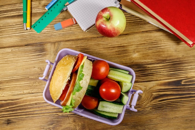 Foto concepto de regreso a la escuela útiles escolares libros manzana y lonchera con hamburguesas y verduras frescas en una mesa de madera vista superior