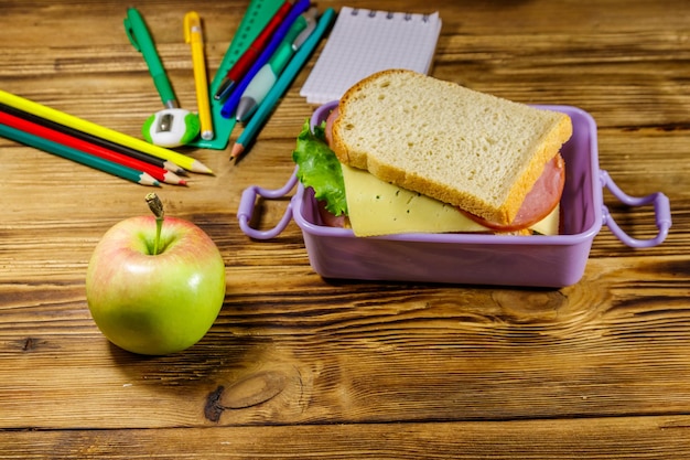 Concepto de regreso a la escuela Útiles escolares manzana y lonchera con sándwiches en un escritorio de madera