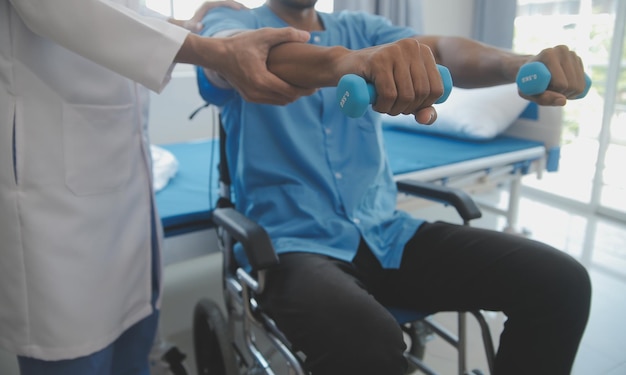 Concepto de rehabilitación de personas discapacitadas Joven fisioterapeuta que ayuda a un paciente masculino mayor en silla de ruedas a hacer ejercicio en casa Anciano discapacitado entrenando con pesas