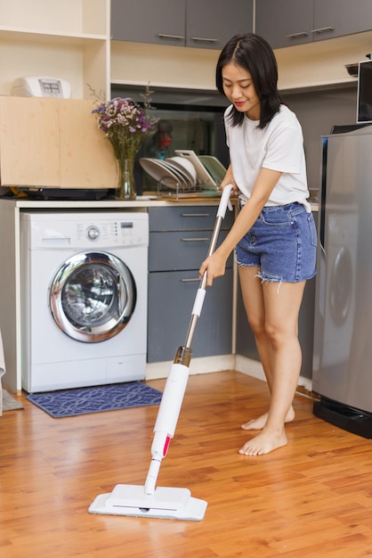 Concepto de relajación en el hogar Mujer joven que usa un trapeador para limpiar el piso en la cocina en casa