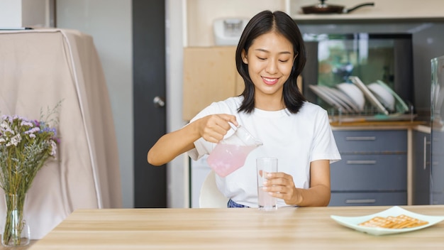 Concepto de relajación en el hogar Mujer joven vierte agua de una jarra en un vaso mientras toma un refrigerio en casa