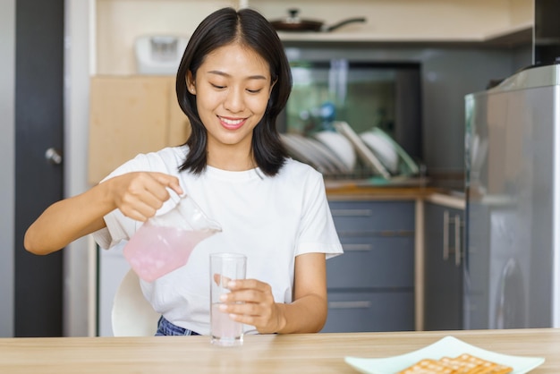 Concepto de relajación en el hogar Mujer joven vierte agua de una jarra en un vaso mientras toma un refrigerio en casa