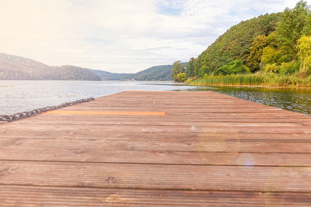 Concepto de relax de turismo de pesca. Hermoso bosque lago o río en un día soleado de verano y antiguo muelle o muelle de madera rústica