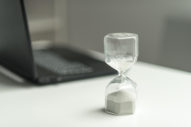 Concepto de reloj de arena cerca de la computadora portátil para la gestión del tiempo y la cuenta atrás a la fecha límite
