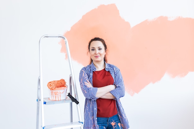 Foto concepto de renovación, redecoración y reparación - pared de pintura de mujer alegre en casa nueva.