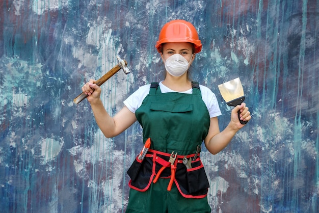 Concepto de renovación y remodelación. mujer con casco y máscara protectora posando con martillo y espátula