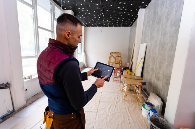 Foto concepto de reparación, construcción y construcción: trabajador sonriente feliz o constructor con computadora de tablet pc y herramientas sobre la construcción