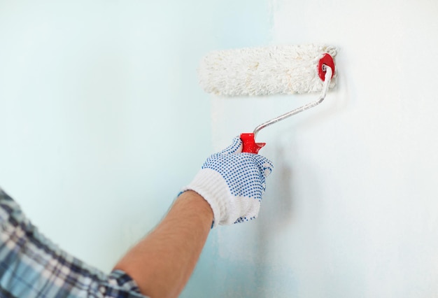 concepto de reparación, construcción y hogar - cierre de macho en guantes pintando pared con rodillo