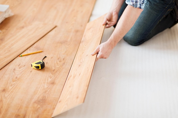 concepto de reparación, construcción y hogar: cierre de manos masculinas que instalan pisos de madera