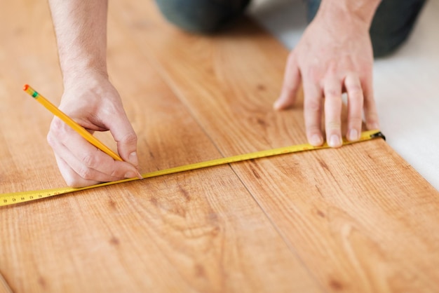 concepto de reparación, construcción y hogar - cierre de manos masculinas que miden suelos de madera