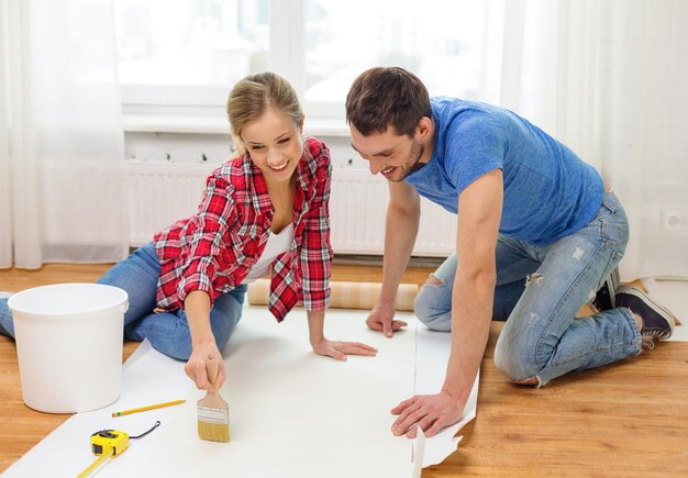 concepto de reparación, construcción y hogar - pareja sonriente manchando papel tapiz con pegamento